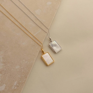 Gold and silver rectangular shell locket necklaces on a textured stone display