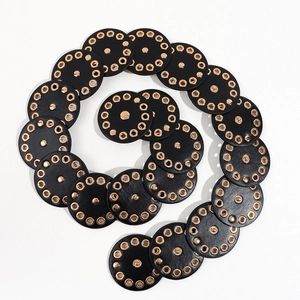 Detail of a black punk waist belt with overlapping round discs and gold metal eyelets