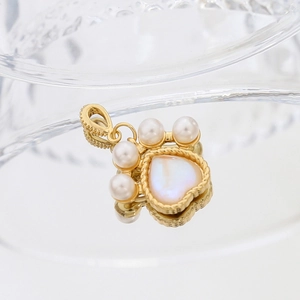 Gold-plated cat paw pendant with heart moonstone and pearl accents on glass surface