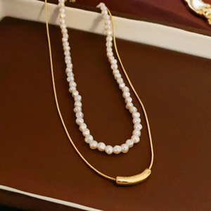 Detail view of double-layer necklace with white pearls and gold curved tube pendant