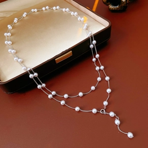 Detailed view of a layered silver necklace featuring elegant white pearls on a gift box