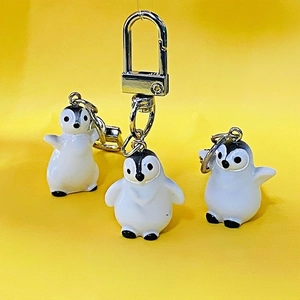 Set of three cute 3D resin penguin keychains with metal ring on yellow background
