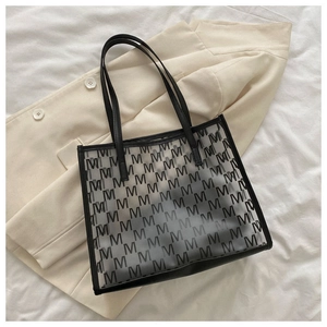 Macro detail of clear PVC tote bag featuring black M letter prints and leather trim