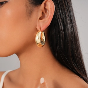 Close-up of golden chunky hoop earrings with a polished finish worn by a model