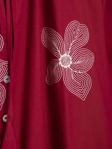 Close-up of white floral embroidery and button details on vintage raspberry red fabric