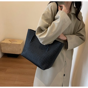 Detailed view of black woven texture tote bag held by a model in a beige trench coat