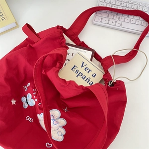 Detail view of red drawstring tote bag featuring colorful embroidery and ribbon handles