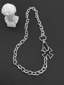 Detail of silver hollow cross pendant with red accents on a chunky cuban chain necklace