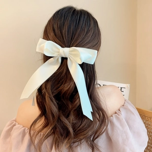 Elegant large cream satin bow hair clip with long ribbons on brunette wavy hair