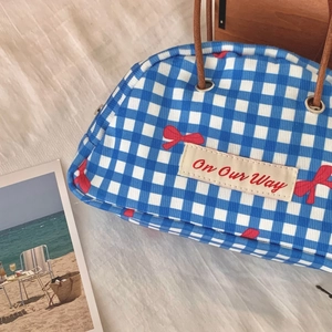 Detail of blue and white checkered handbag with red bow print and leather handle