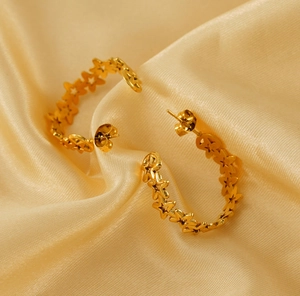 Detailed view of gold stainless steel star cutout hoop earrings on silk background