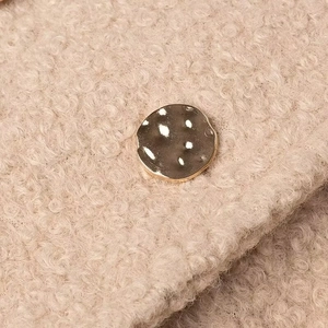 Macro detail of beige sherpa wool coat fabric with a vintage hammered gold metal button