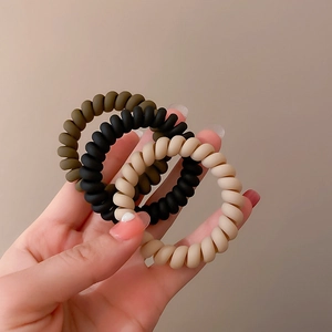 Close-up of matte spiral hair ties in dark green, black, and beige cream colors