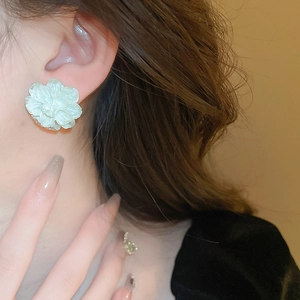 Elegant light green acrylic flower stud earrings worn by a model in warm natural light