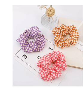 Close-up of three checkered scrunchies in purple, orange, and pink on a bright desk