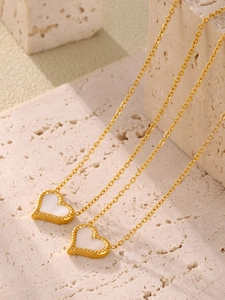 Detailed macro shot of a gold heart necklace with white mother-of-pearl inlay and beaded edges