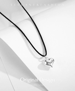 Close-up of polished silver heart pendant on a minimalist black cord necklace