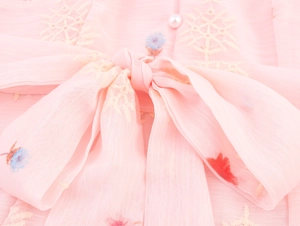 Detail van roze chiffon jurk met grote strik, parelmoer knoop en bloemenborduurwerk