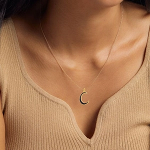 Detailed close-up of a golden crescent moon necklace with black inlay on a female model
