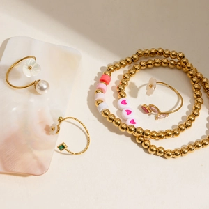 Detail of adjustable gold ring set featuring pearls and floral charms on marble surface