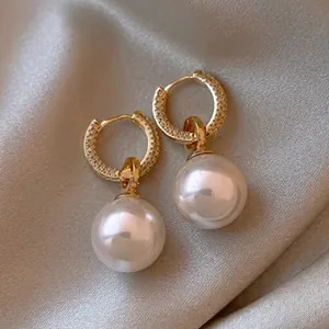 Close-up of gold crown earrings with micro-pave diamonds and large white round pearls