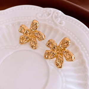 Golden abstract flower stud earrings with hammered texture on a white ceramic plate