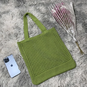Close-up of grass green knit tote bag with hollow crochet patterns and smartphone size reference