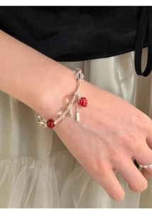 Detailed view of beaded strawberry charm bracelet with red glass beads on female wrist