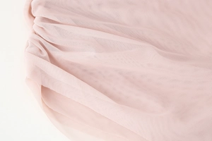 Macro detail of soft pink pleated mesh fabric with fine sheer texture and ruffles