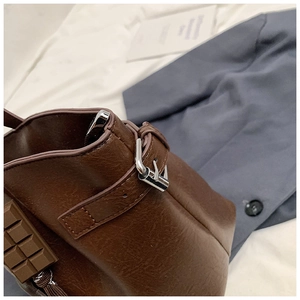Detail of brown leather tote bag with chocolate charm and silver metal buckle