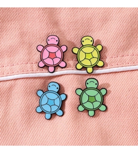 Close-up of four colorful turtle enamel pins in pink, yellow, blue, and green on denim