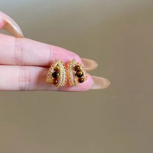 Close-up of vintage gold leaf earrings with zircons and brown tiger eye stone