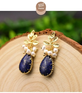 Detailed shot of handmade leaf earrings with pearls and blue lapis lazuli on wood