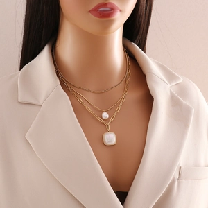 Detailed view of layered gold-tone necklace with pearl and square pendant on a beige suit
