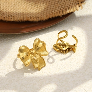 Detailed close-up of 18K gold plated bow and fishbone rings on textured stone surface