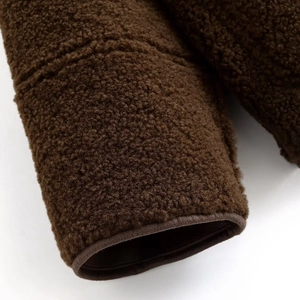 Détail de la manche d'une veste en peluche marron montrant la texture douce et les coutures