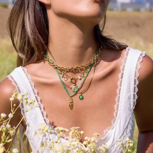 Layered gold chain necklace with green beads and face pendant on a model in nature