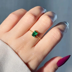 Detailed close-up of emerald-cut green gemstone ring with adjustable 18K gold chain