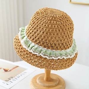 Handcrafted straw sun hat with green plaid lace trim on a minimalist wood stand