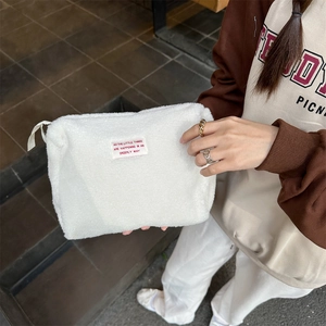 Detail of white faux shearling cosmetic bag with zipper and red embroidered patch