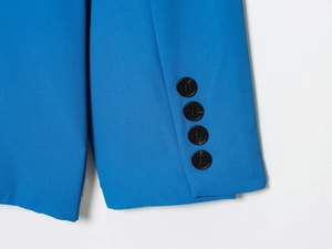 Détail de la manche d'un blazer bleu électrique avec boutons noirs et texture sergé