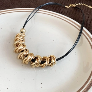 Detail view of twisted gold hoop necklace with black cord on a ceramic plate