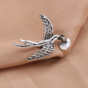 Detailed close-up of retro silver swallow brooch with heart pendant on soft fabric