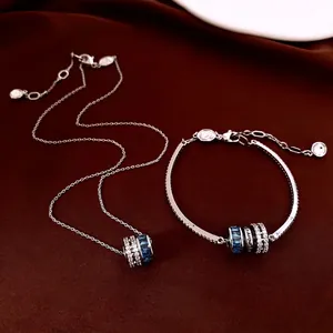 Silver necklace and bracelet set with blue zircon barrel pendant on dark red velvet