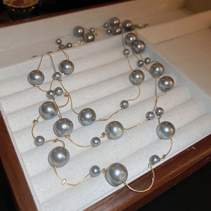 Detail of layered grey pearl necklace on a beige velvet tray with gold chain elements