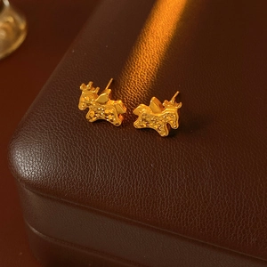 Close-up of golden deer stud earrings with textured finish on a dark brown leather box