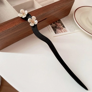 Elegant wavy black hair pin with white flowers and gold stamens on a wooden box