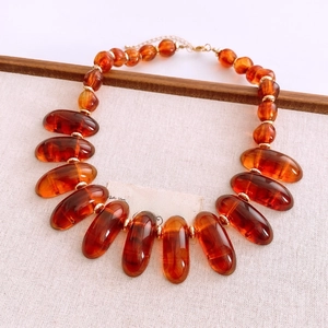 Close-up of amber oval acrylic beads on beige linen with a gold lobster clasp