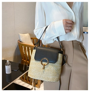 Detail of beige straw bucket bag featuring a black leather flap and gold ring hardware