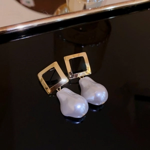 Macro shot of gold square stud earrings with irregular baroque pearls on black surface